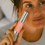 Person holding a pink lip balm with a brand logo close to their face.