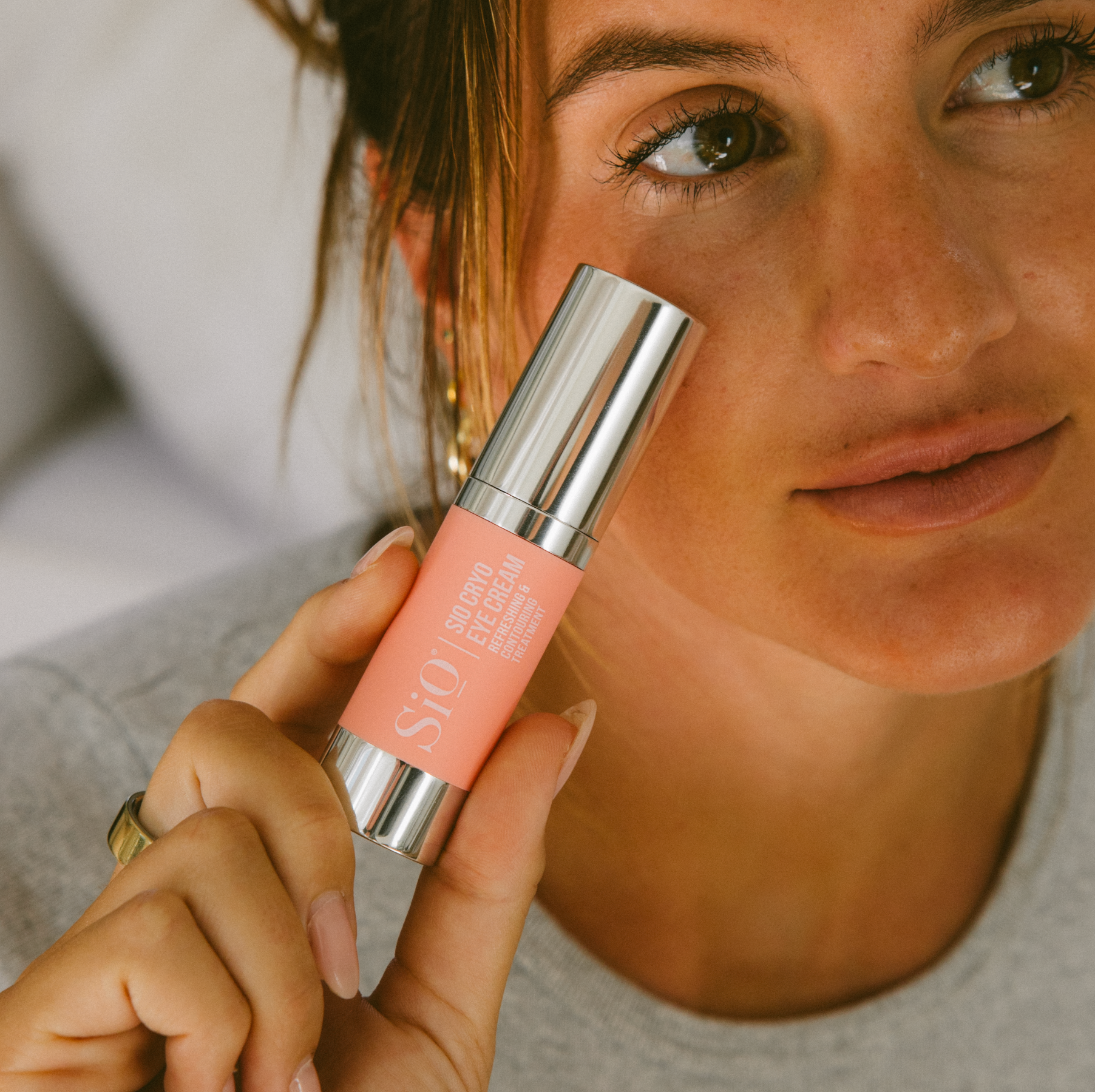 Person holding a pink lip balm with a brand logo close to their face.