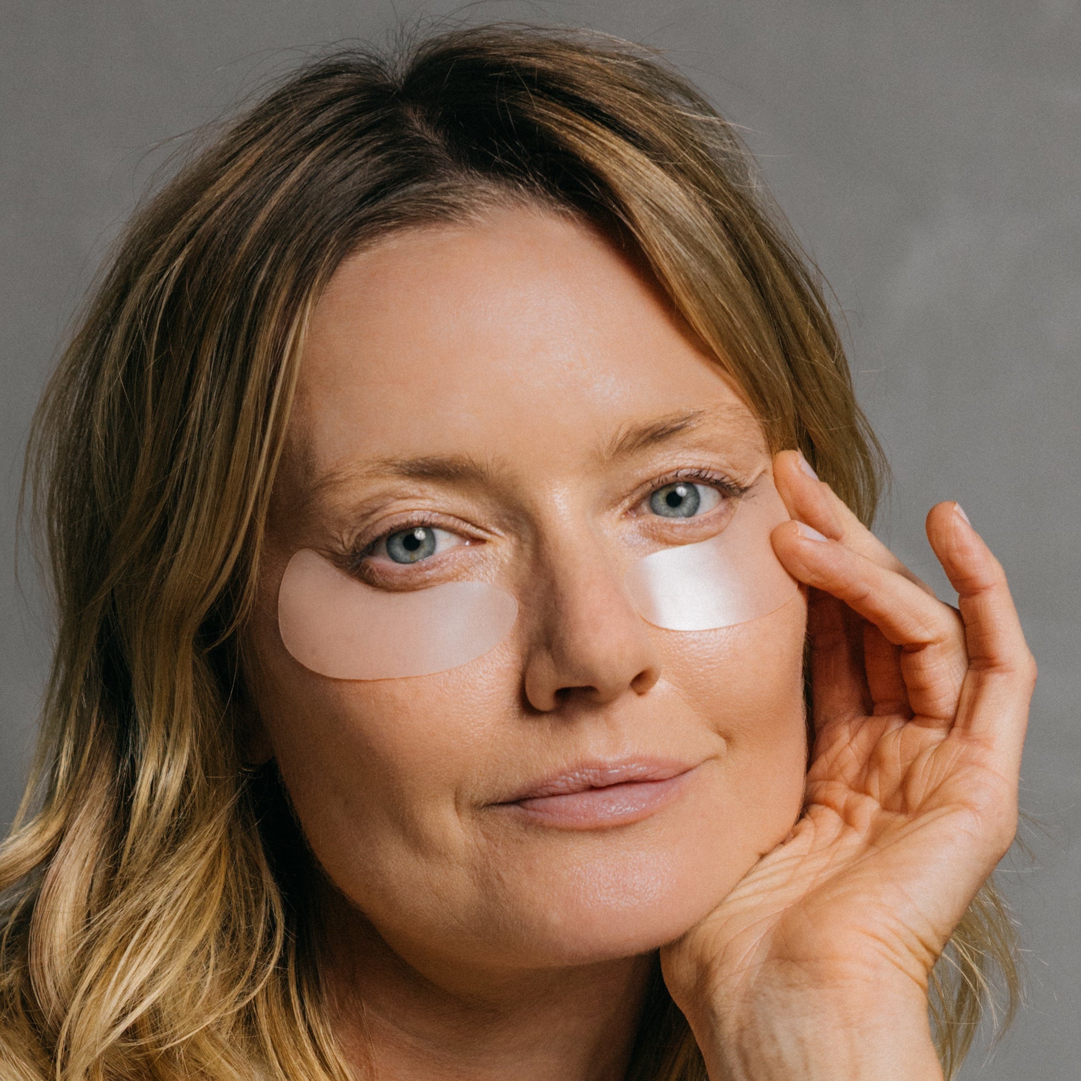 Woman applying eye patches with a neutral background