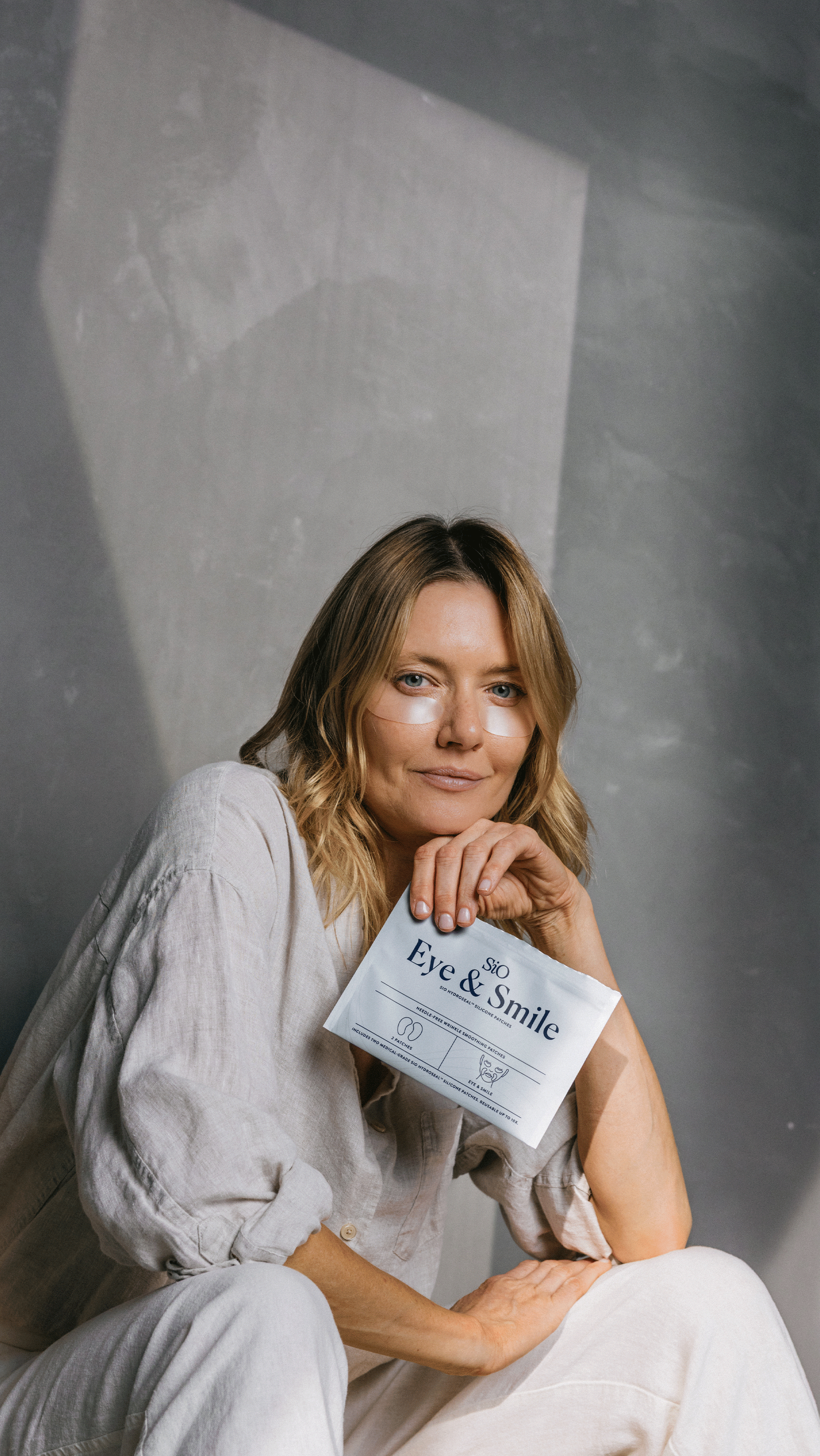 Woman holding a product labeled 'Eye & Smile' against a gray background