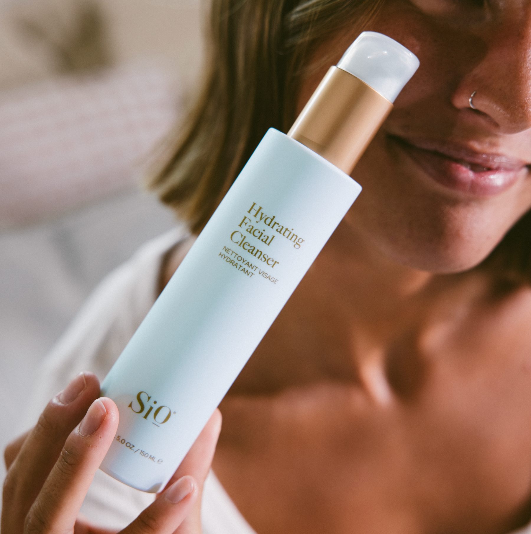 Person holding a 'Hydrating Facial Cleanser' by SiO with a blurred background