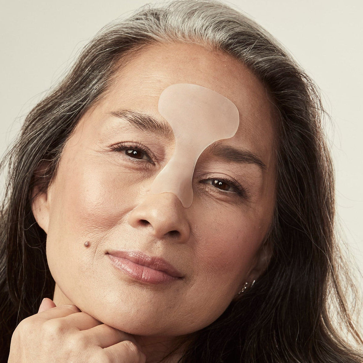 Woman with a skincare patch on her face against a plain background