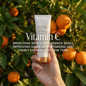 SIO Beauty Multivitamin Face & Body Scrub tube held by hand with oranges in background. Brightens skin and evens tone.